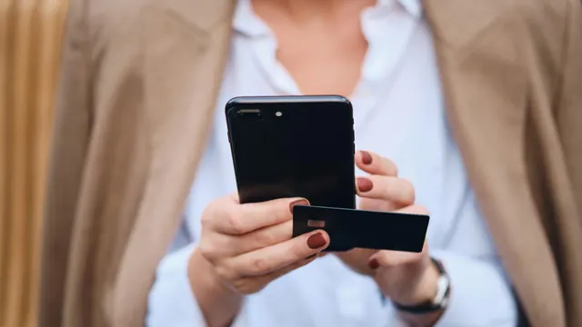 Businesswoman holding a smartphone and a payment card (stock photo, illustrative)